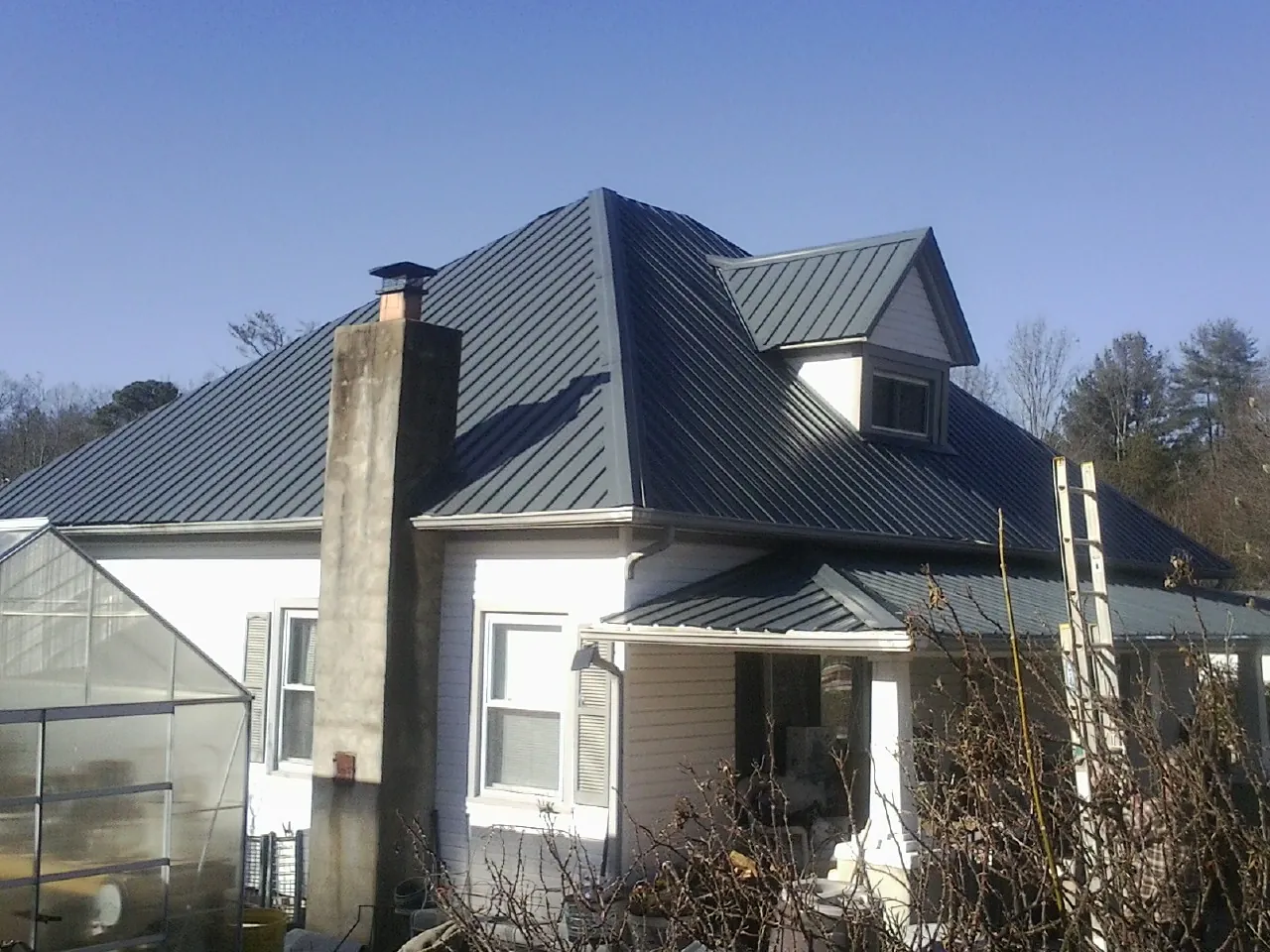 Dark blue standing seam metal roof on a white farmhouse with dormer — Slate & Tile Roof Repair by Roofing Brothers in Ostrander