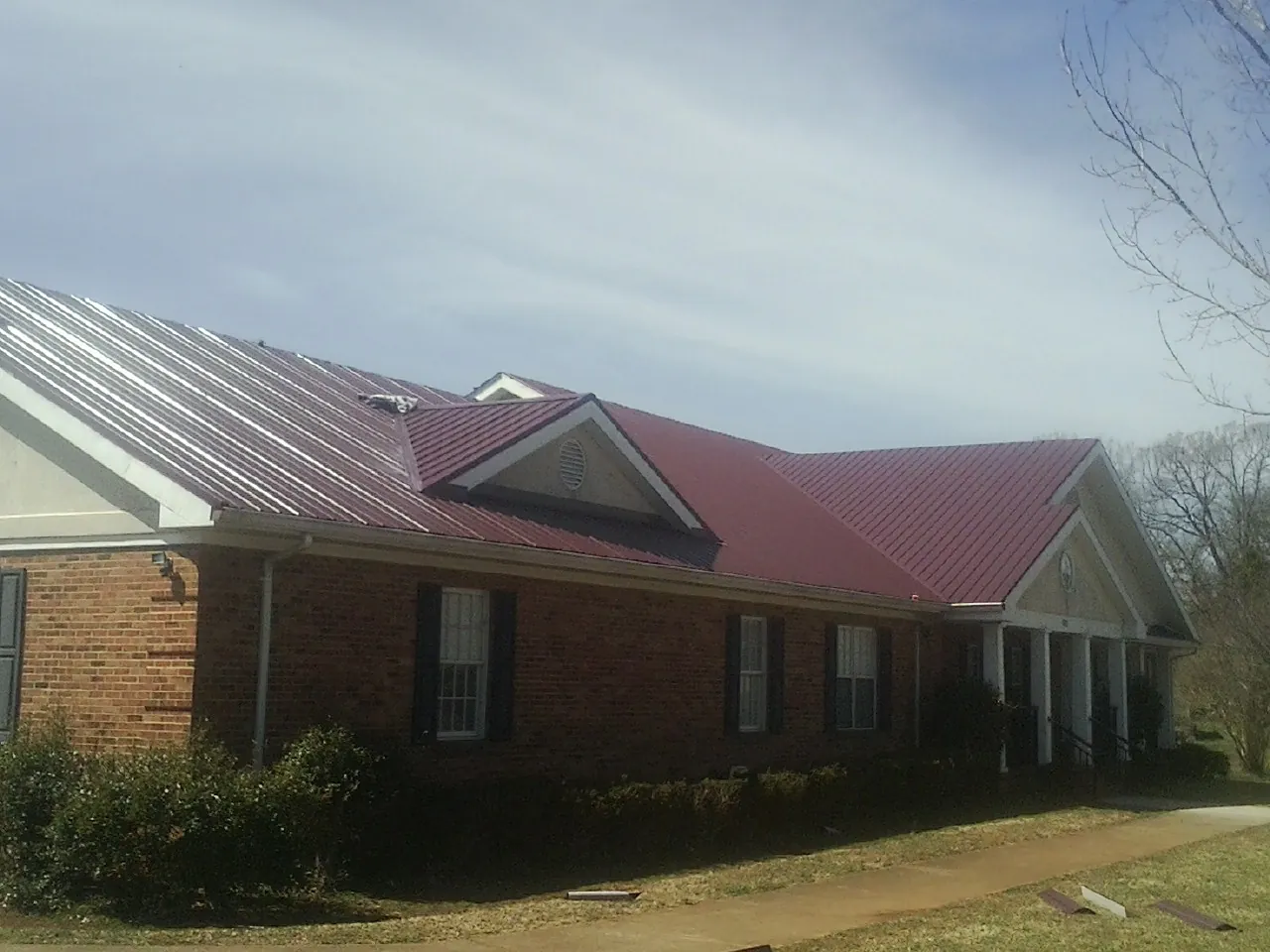 Red metal roof with gabled entries on a long brick building, from a Hail Damage Roof Repair job in Ostrander