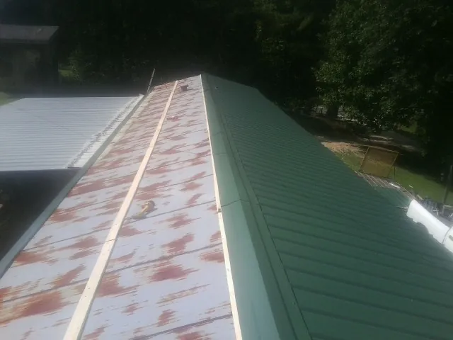 Old rusted panels beside newly installed green metal roofing — Wind Damage Roof Repair by Roofing Brothers in Ostrander