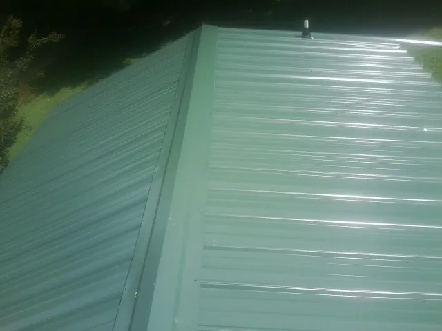 New green metal panels meeting at the ridge of a roof — Flat Roof Repair work by our crew in Ostrander
