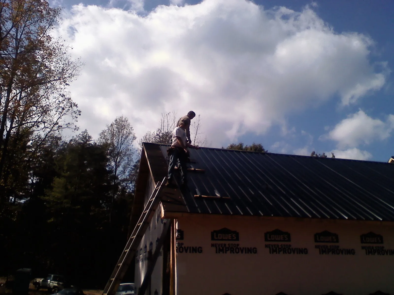 Roofer fastening dark metal panels high against a cloudy sky, from a Roof Inspection job in Ostrander