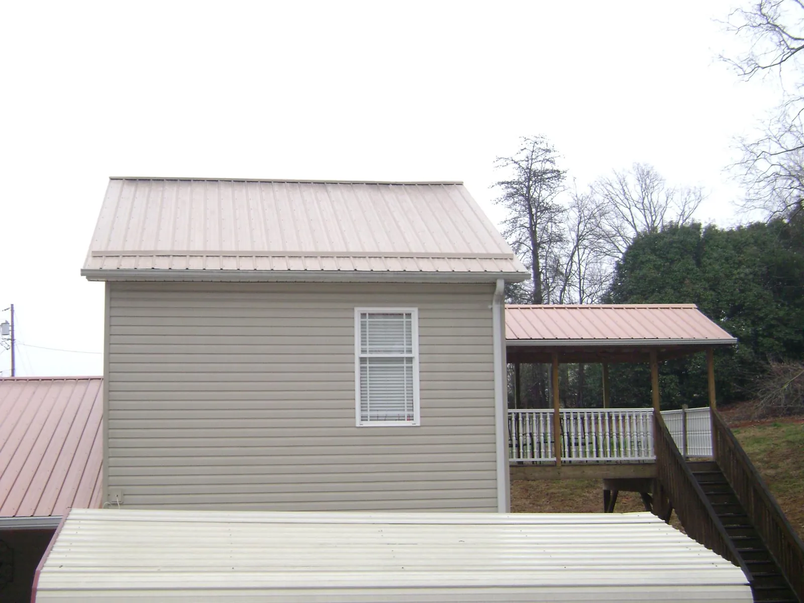 Tan metal roofs on a two story addition and attached porch, from a Roof Replacement job in Ostrander