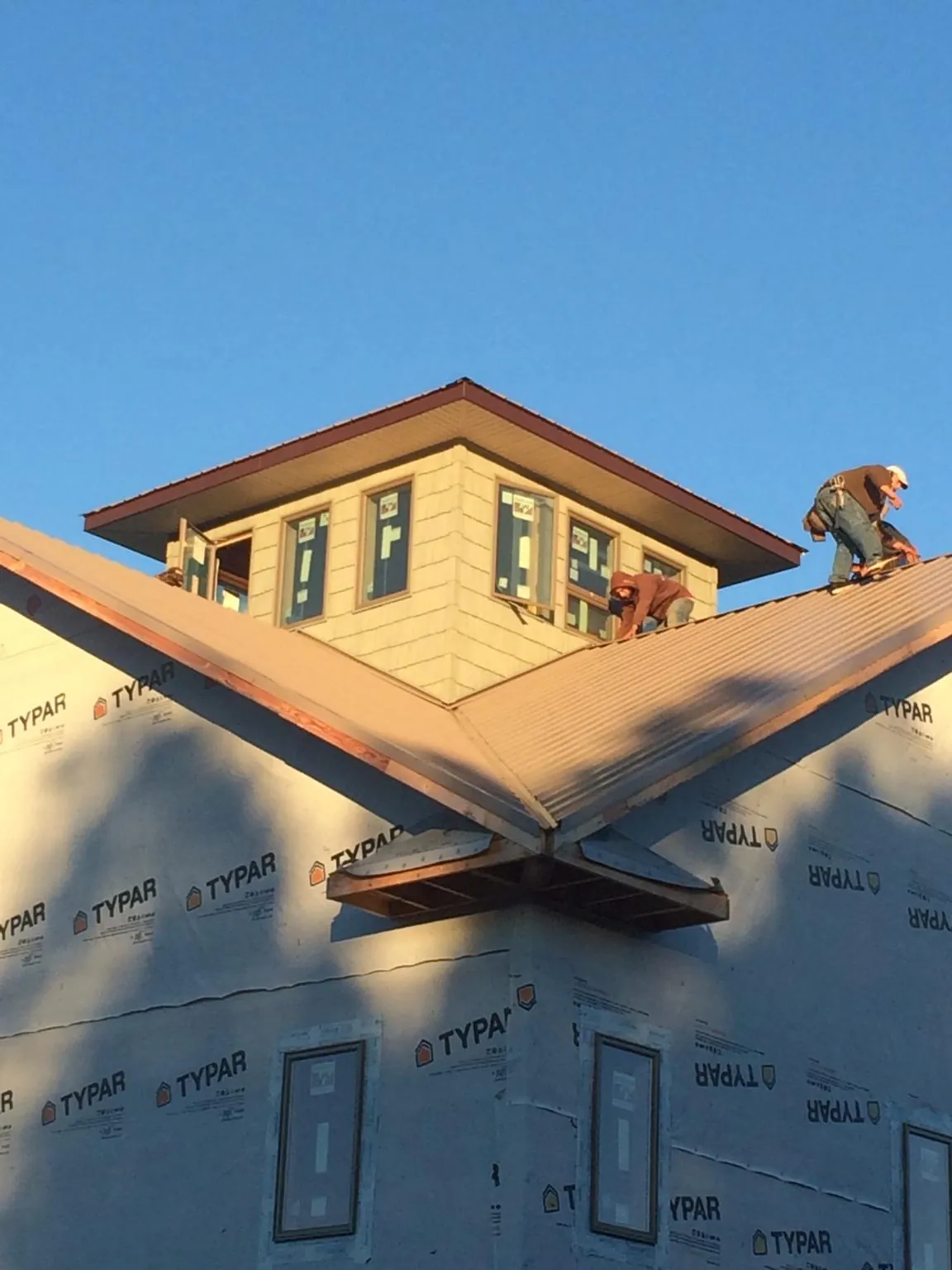 Roofers working around a rooftop cupola on a new metal roof at sunset — Roof Waterproofing in Ostrander by Roofing Brothers